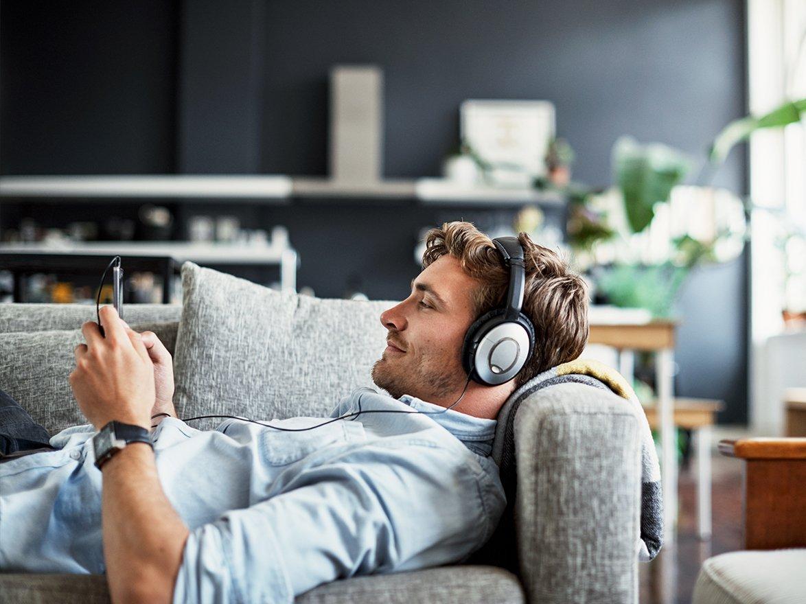 Man laying on sofa with headphones on looking at mobile phone