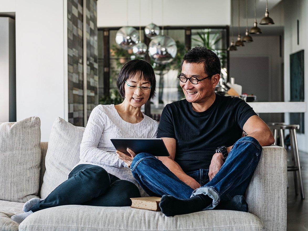 Couple sitting on sofa looking at tablet and smiling